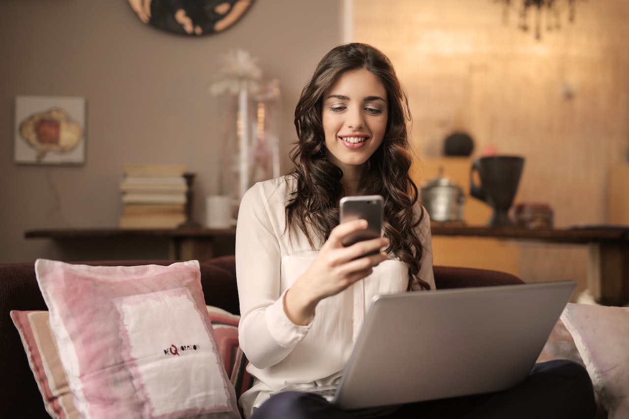 Woman Sitting on Sofa While Looking at Phone With Laptop | IBOMMA TV
