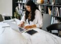 Ethnic lady working remotely on netbook at table in room | IBOMMA TV