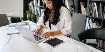Ethnic lady working remotely on netbook at table in room | IBOMMA TV